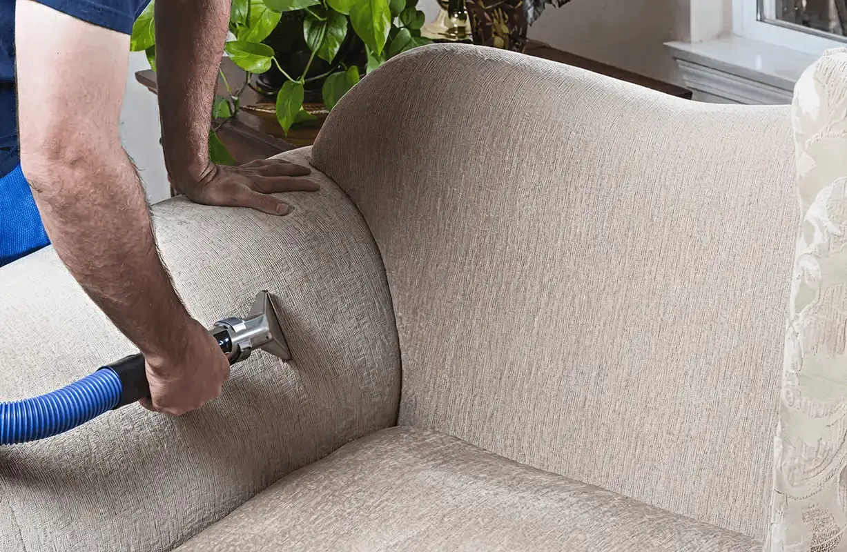 Professional upholstery cleaner deep-cleaning a fabric sofa with a handheld extraction tool and hose, Atlanta, GA.
